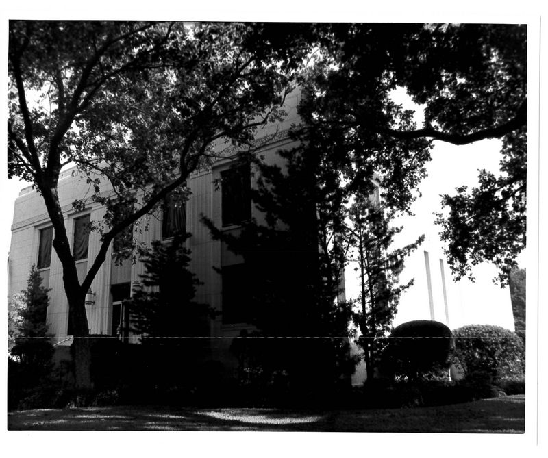 Black and white photo of white building behind trees.