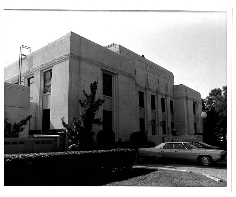 Black and white photo of white building with cars from the 50s in front of it.